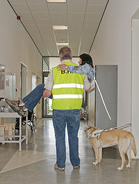 Een BHV'er tilt een persoon met visuele beperking op